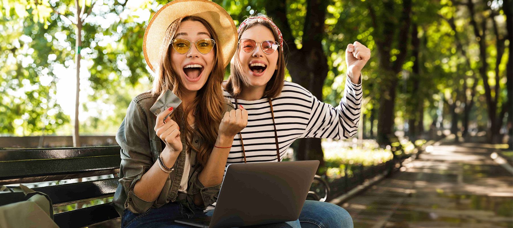 Photo of young emotional excited happy ladies friends outdoors sitting using laptop computer holding credit card.